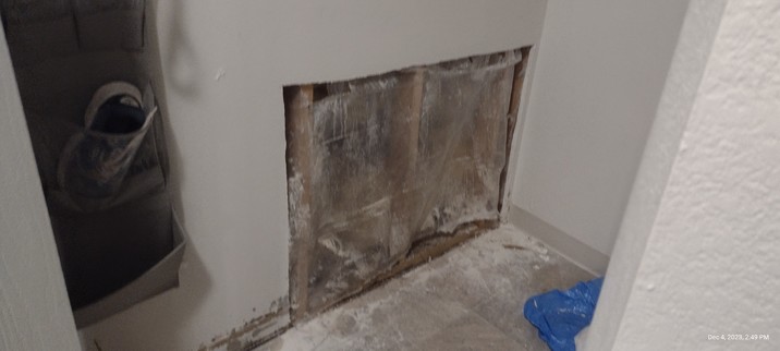 View of inside entryway closet shows a large square hole cut into drywall
 Dust and dirt are on the floor beneath it. 

The hole is covered with clear plastic 